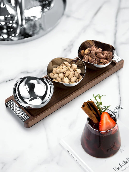 Metal bowls on a wooden tray with a glass of red wine and garnishes on a marble surface.