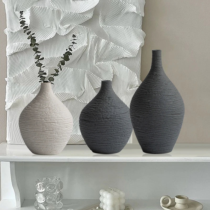 Three gray textured vases on a white shelf with abstract wall art in the background.