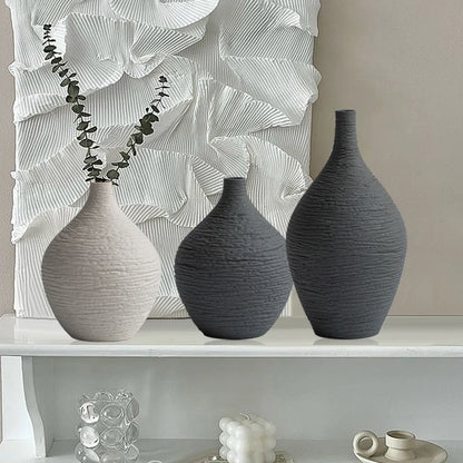 Three gray textured vases on a white shelf with abstract wall art in the background.