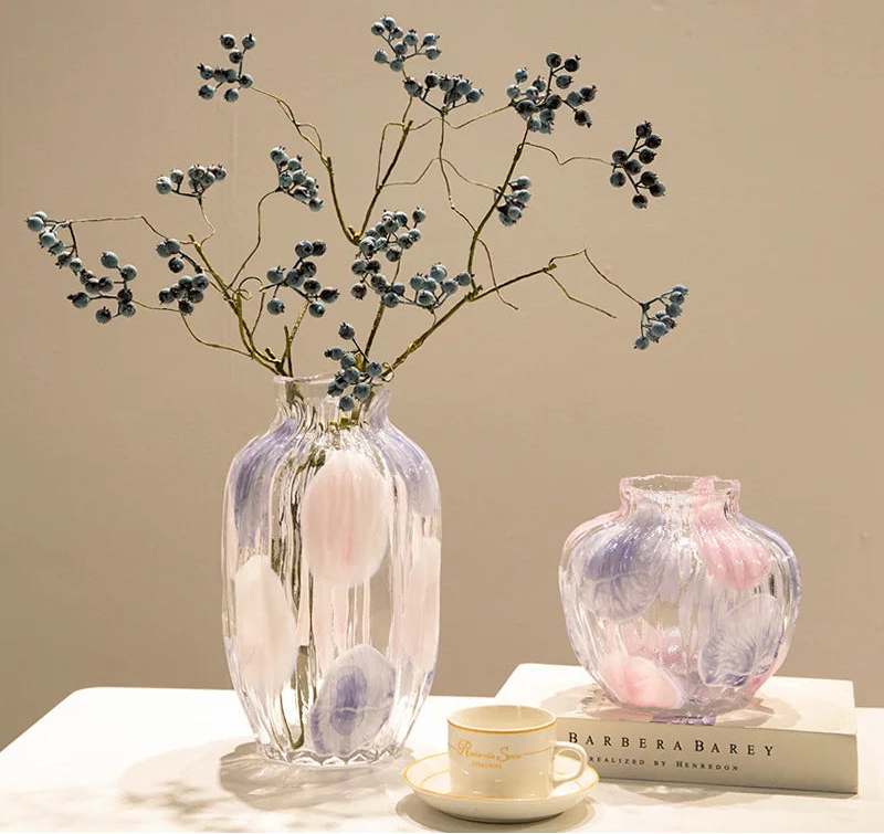 Decorative glass vases with floral branches on a table against a beige wall.