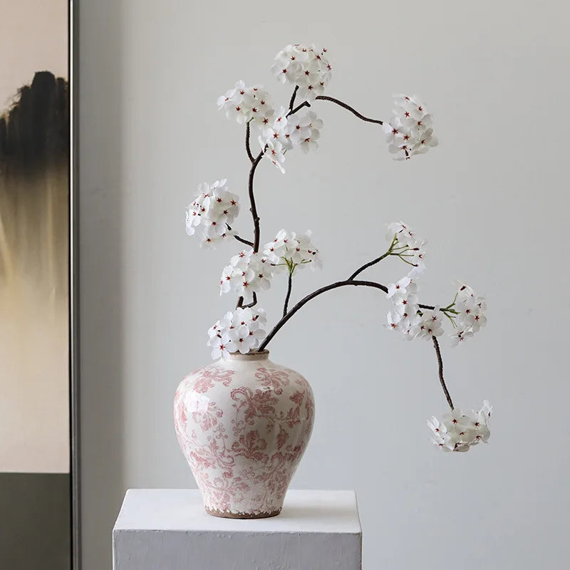 Decorative vase with floral branches on a white surface against a light gray wall.
